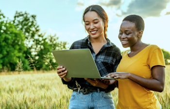 two people holding a laptop computer in a grassy field